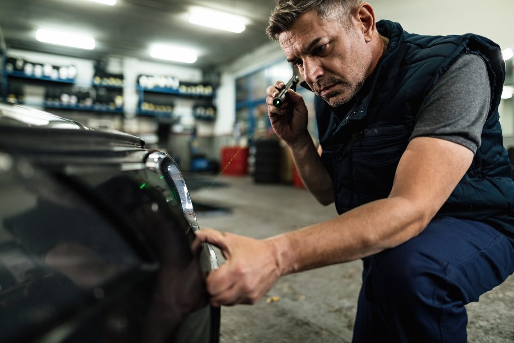 auto mechanic examining front bumper in repair shop.